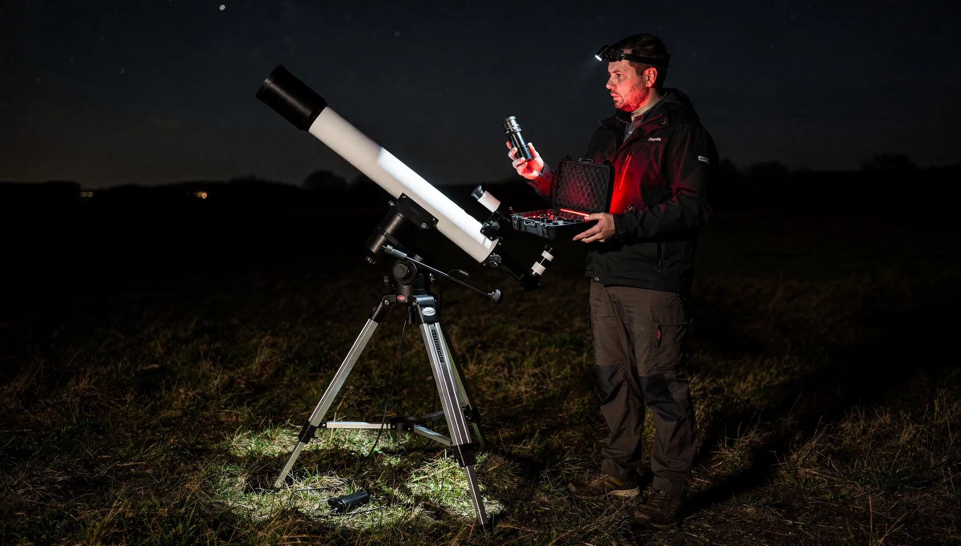 Astronome tenant un oculaire près d’une lunette astronomique sur trépied, de nuit.